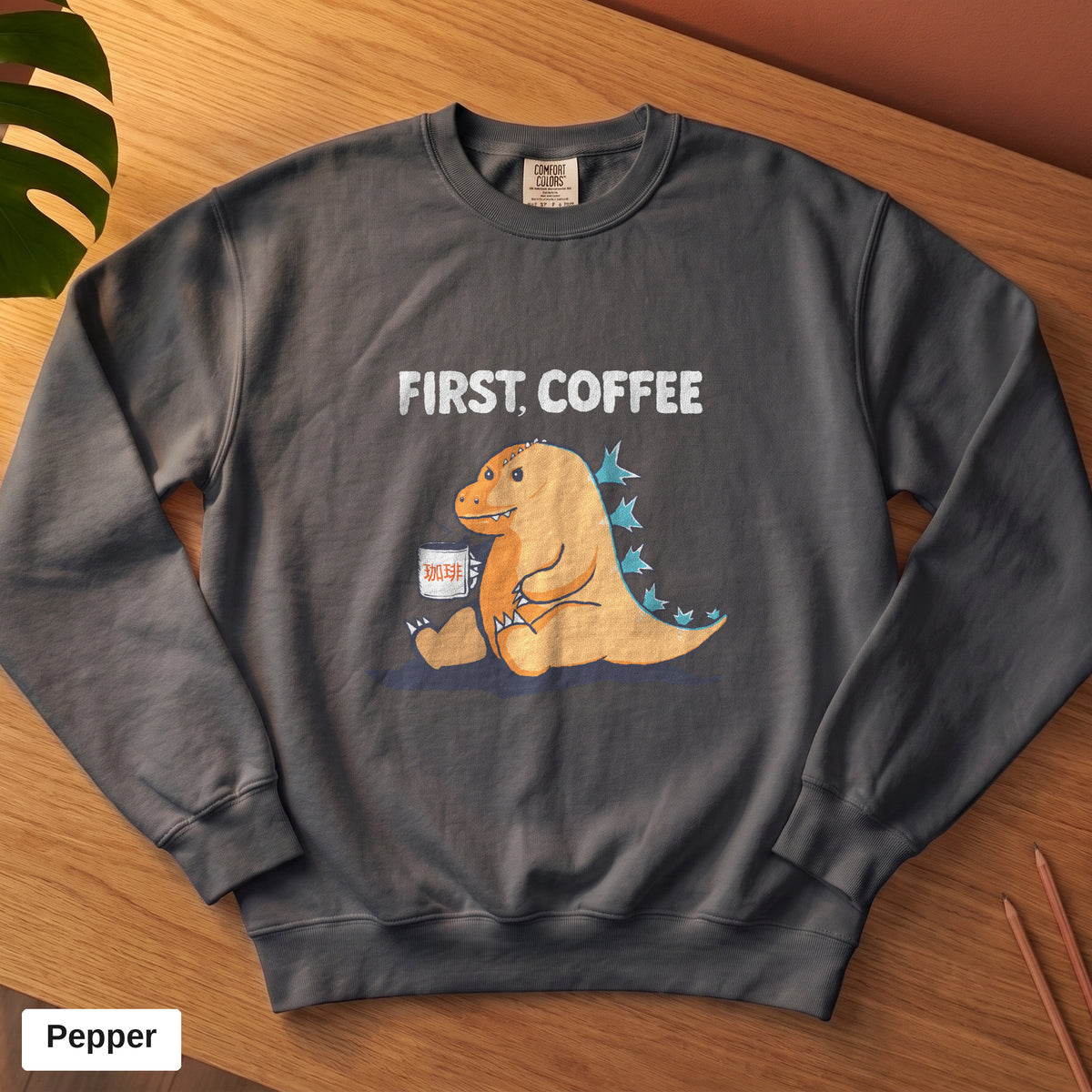 Pepper Comfort Colors crewneck sweatshirt, folded flat lay, First Coffee kaiju design printed on the chest
