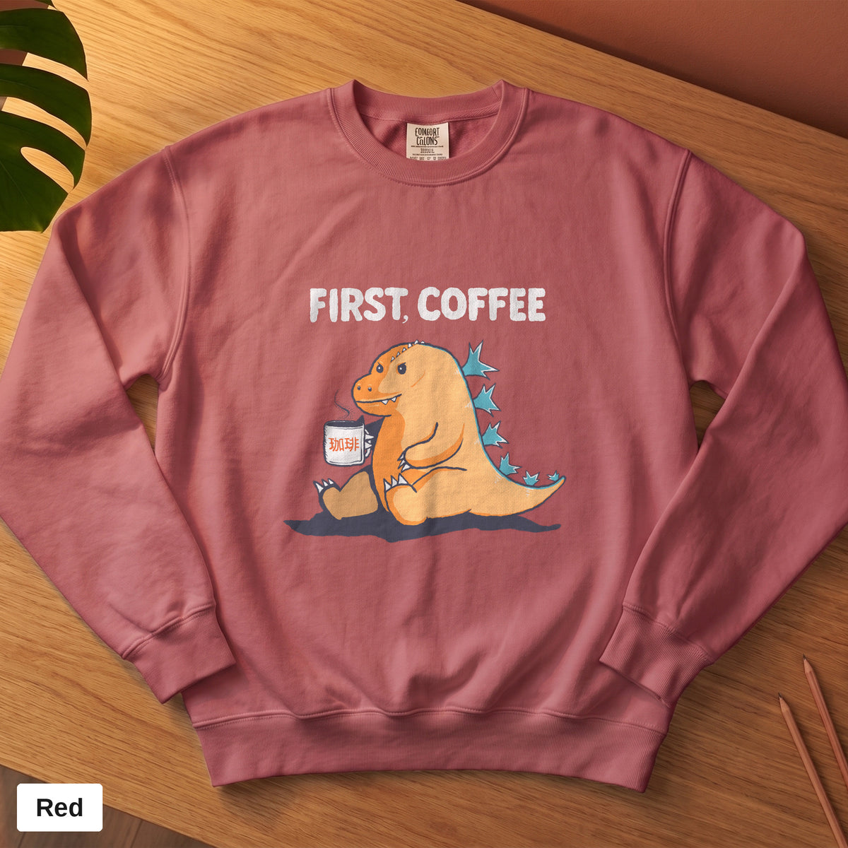 Crimson Comfort Colors crewneck sweatshirt, folded flat lay, First Coffee kaiju design printed on the chest