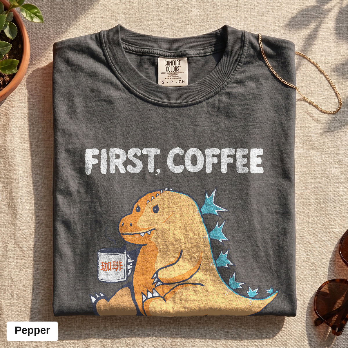 First Coffee dinosaur graphic tee, Comfort Colors 1717 in Pepper, folded flat lay