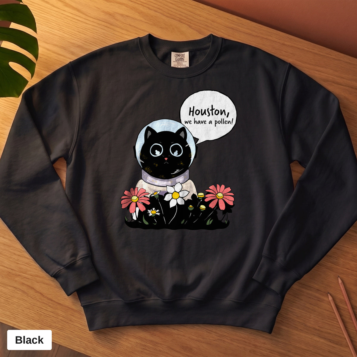 Black Comfort Colors crewneck sweatshirt, folded flat lay, Houston We Have A Pollen cat astronaut design printed on the chest