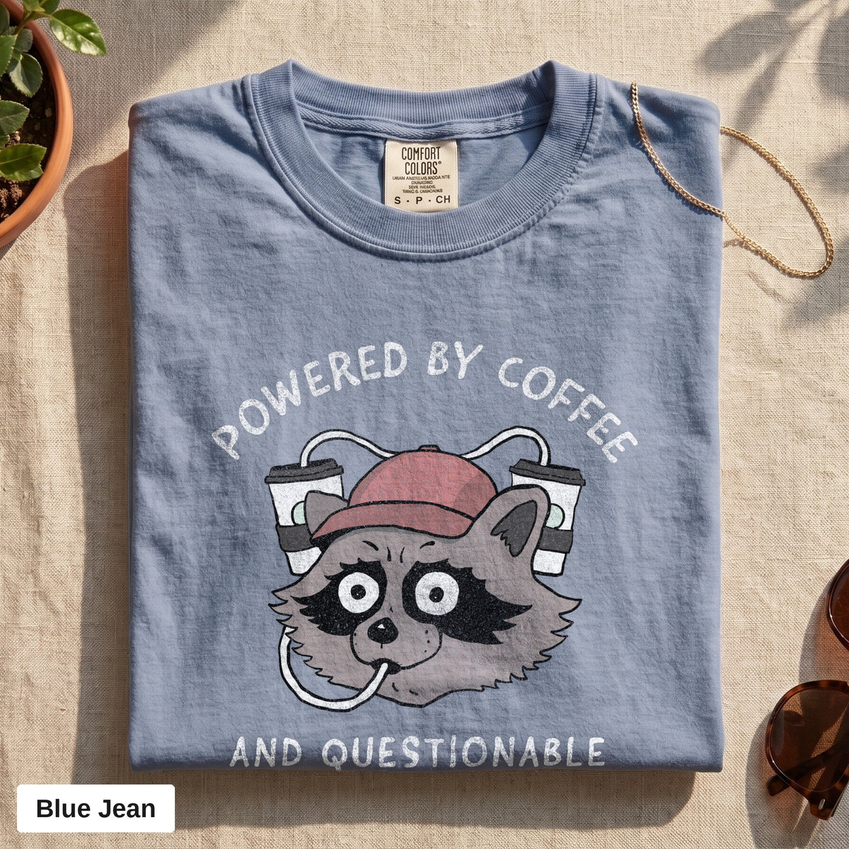 Powered By Coffee And Questionable Life Choices raccoon tee, Comfort Colors 1717 in Blue Jean, folded flat lay
