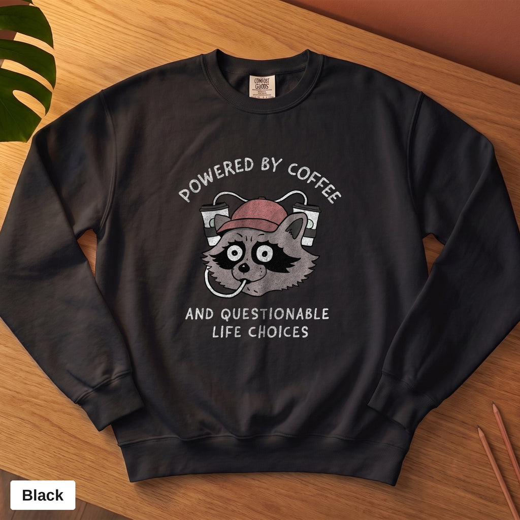 Black Comfort Colors crewneck sweatshirt, folded flat lay, Powered By Coffee And Questionable Life Choices raccoon design printed on the chest