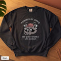 Black Comfort Colors crewneck sweatshirt, folded flat lay, Powered By Coffee And Questionable Life Choices raccoon design printed on the chest
