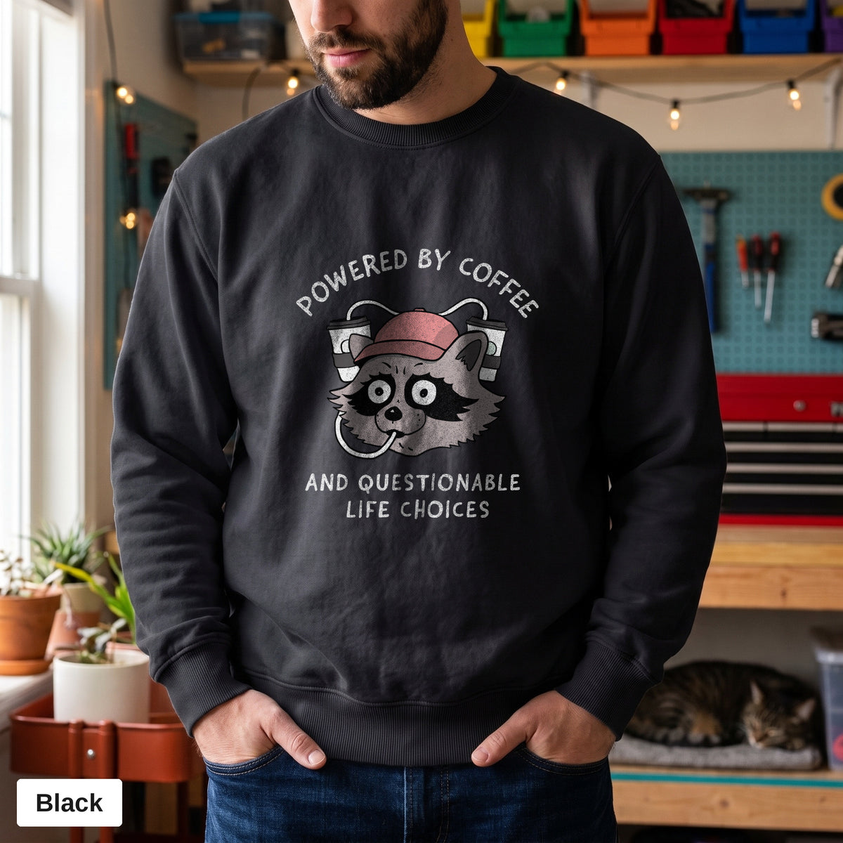 Black Comfort Colors crewneck sweatshirt worn by a man, Powered By Coffee And Questionable Life Choices raccoon design printed on the chest