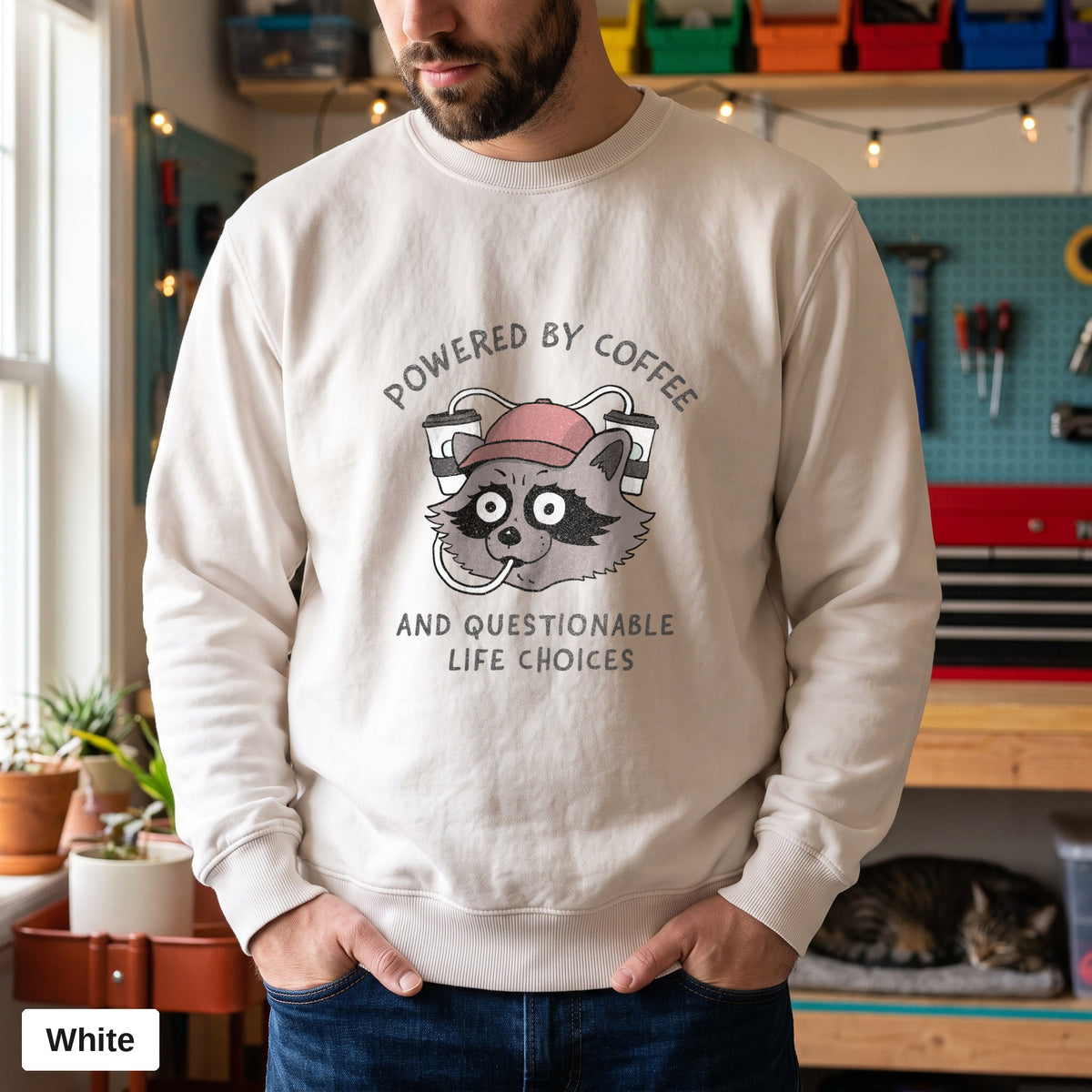 White Comfort Colors crewneck sweatshirt worn by a man, Powered By Coffee And Questionable Life Choices raccoon design printed on the chest