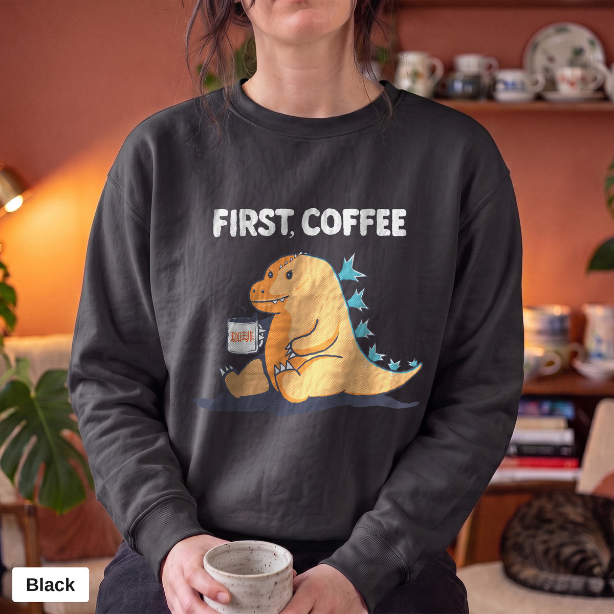 Black Comfort Colors crewneck sweatshirt worn by a model, First Coffee kaiju design printed on the chest