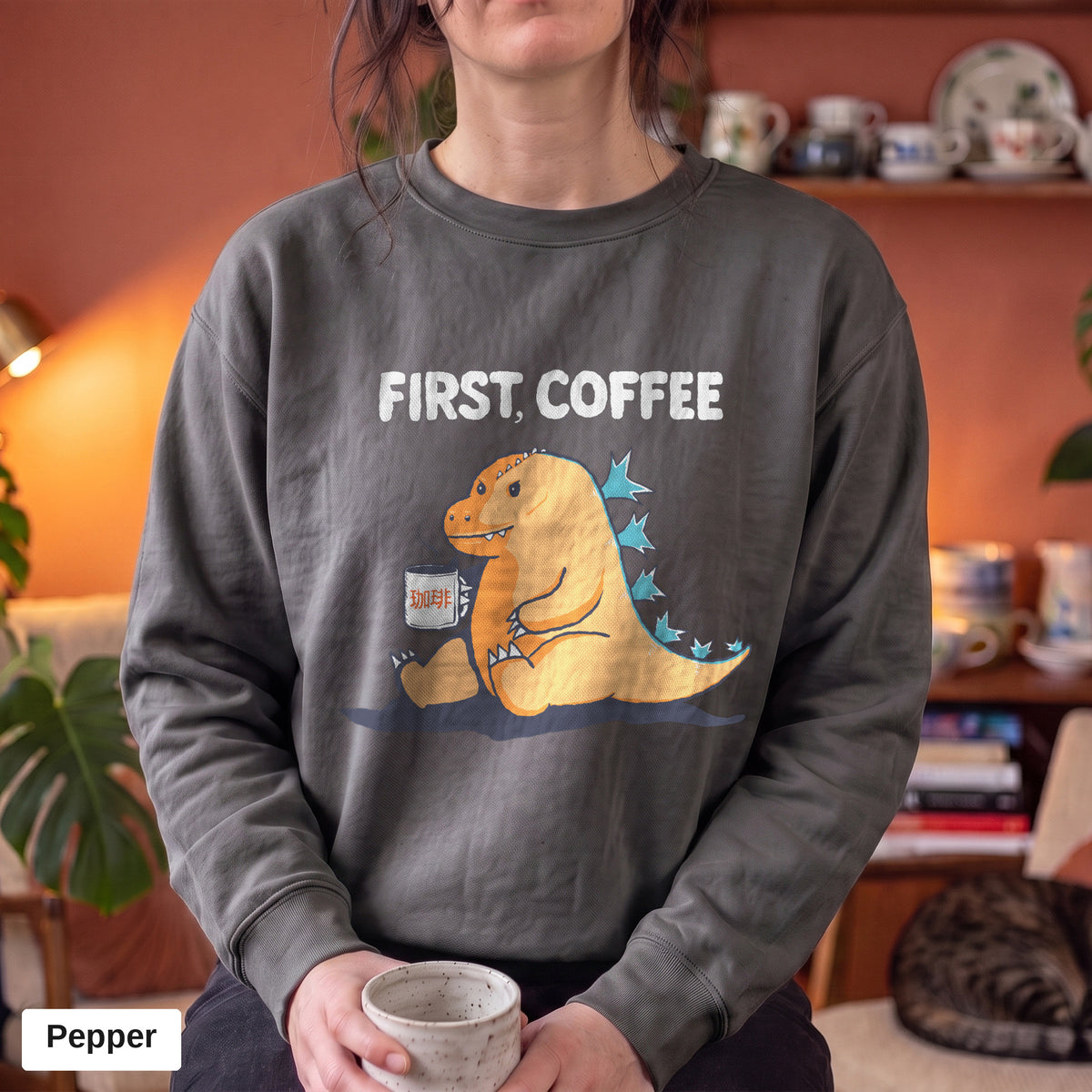 Pepper Comfort Colors crewneck sweatshirt worn by a model, First Coffee kaiju design printed on the chest