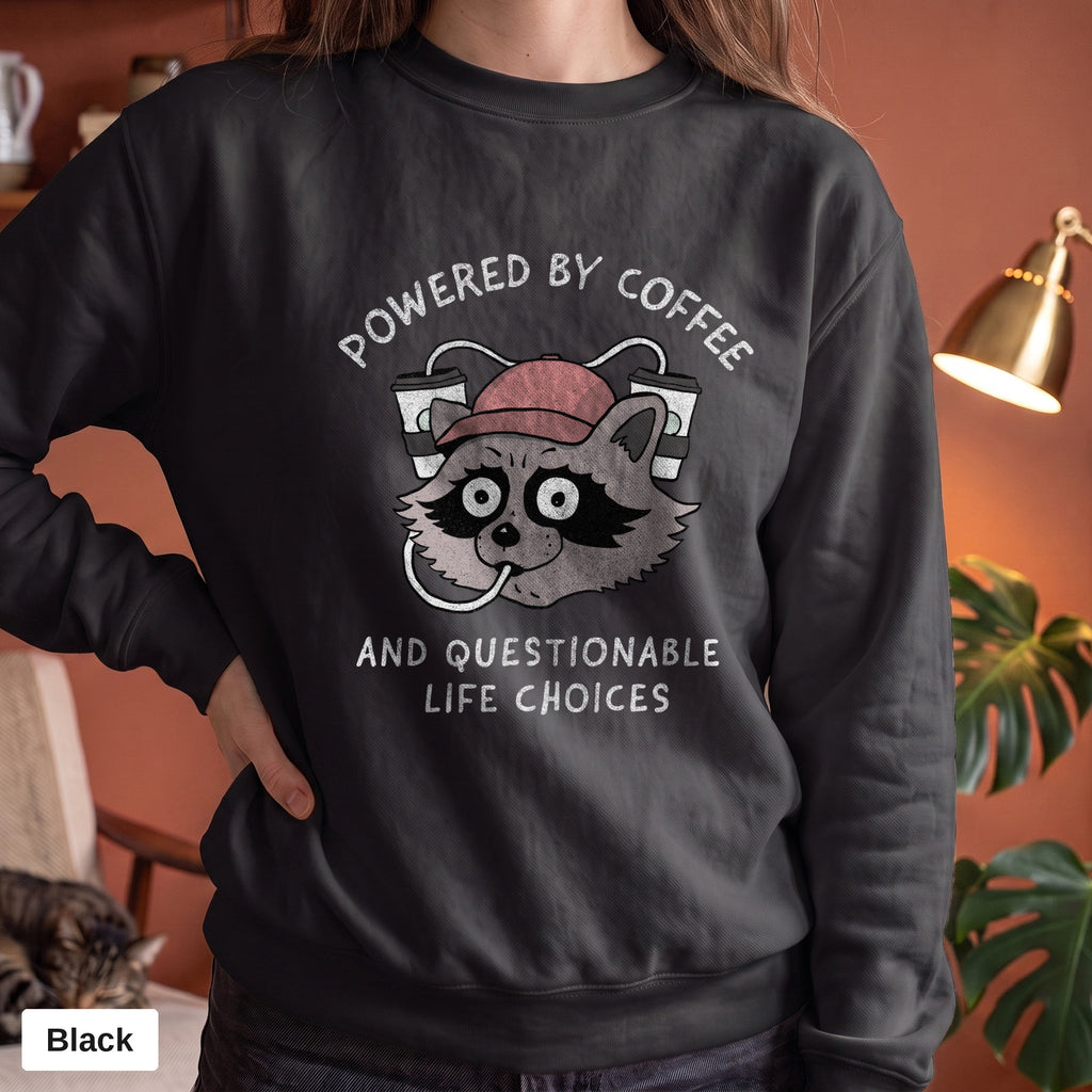 Black Comfort Colors crewneck sweatshirt worn by a model, Powered By Coffee And Questionable Life Choices raccoon design printed on the chest