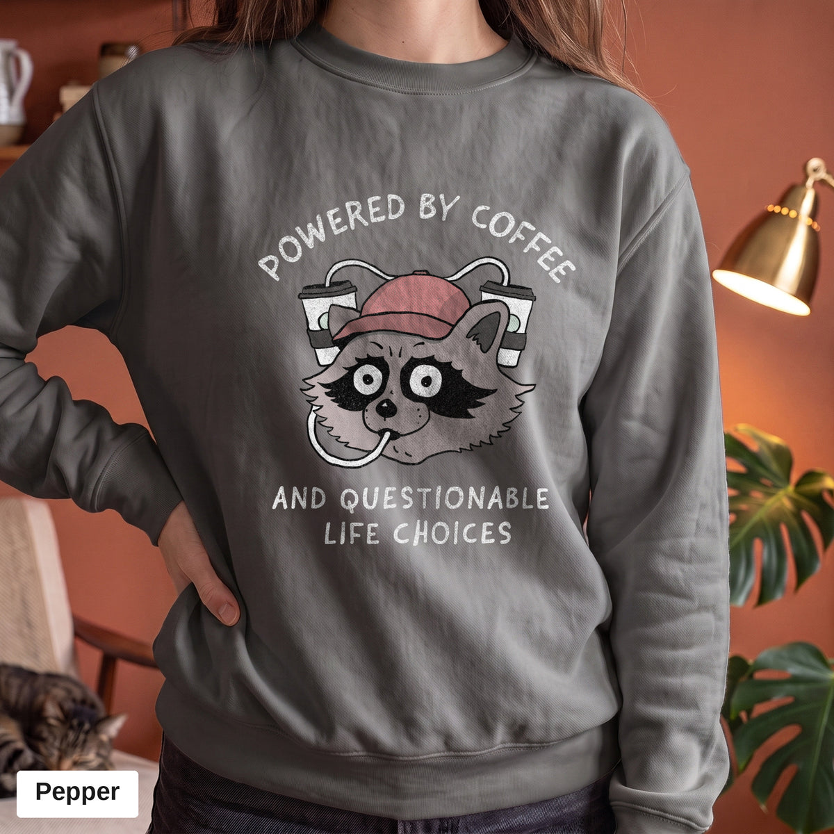 Pepper Comfort Colors crewneck sweatshirt worn by a model, Powered By Coffee And Questionable Life Choices raccoon design printed on the chest