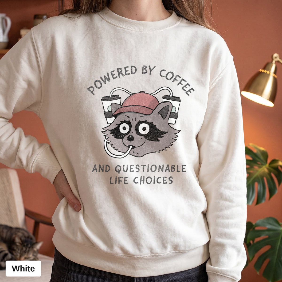 White Comfort Colors crewneck sweatshirt worn by a model, Powered By Coffee And Questionable Life Choices raccoon design printed on the chest